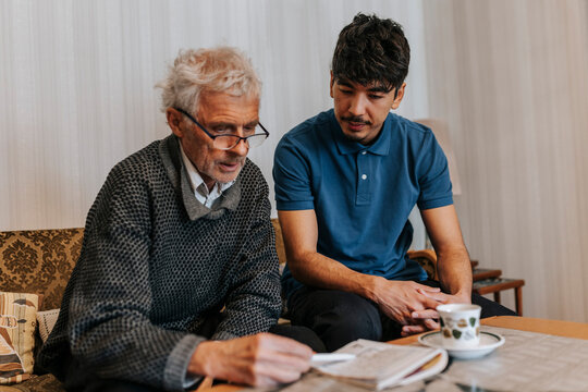 Male caregiver sitting with senior man playing Sudoku at home