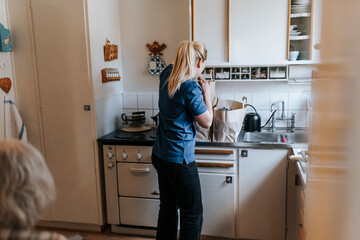 Female caregiver unpacking groceries while standing in kitchen at home