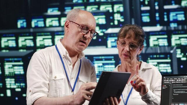 Software developers in high tech establishment, completing tasks on tablet while running scripts on laptop terminal. Proactive programmers amidst server rows, accessing databases and manipulating code