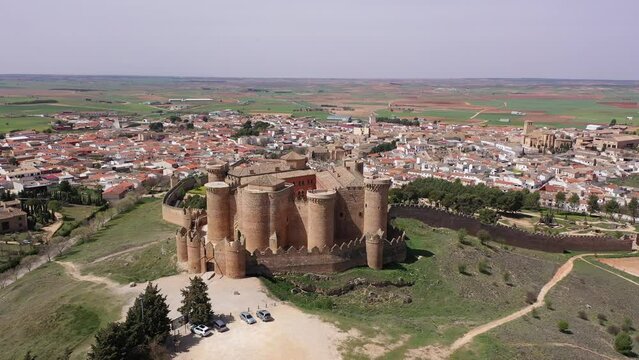 View from drone of Castillo de Belmonte, ancient walled fortified castle on background of townscape and extensive agricultural fields on sunny spring day, Spain