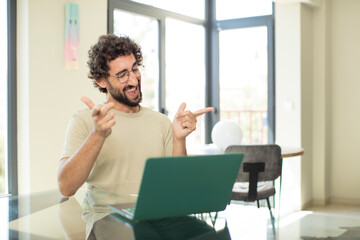 young adult bearded man with a laptop feeling happy, cool, satisfied, relaxed and successful, pointing at camera, choosing you