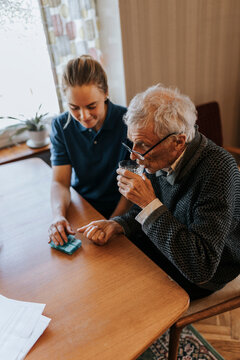 High angle view of senior man taking medicines while sitting with female caregiver at home