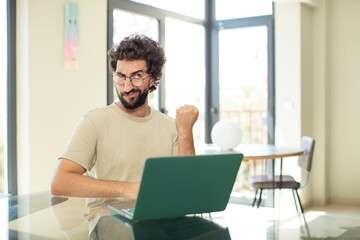 young adult bearded man with a laptop looking confident, angry, strong and aggressive, with fists ready to fight in boxing position