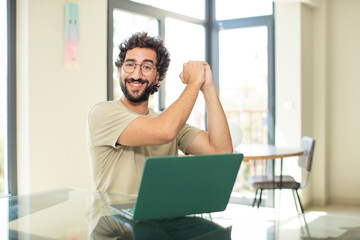 young adult bearded man with a laptop feeling happy, surprised and proud, shouting and celebrating success with a big smile