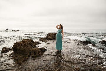 Pregnant woman posing in the long dress at Andalusian coast next to the sea