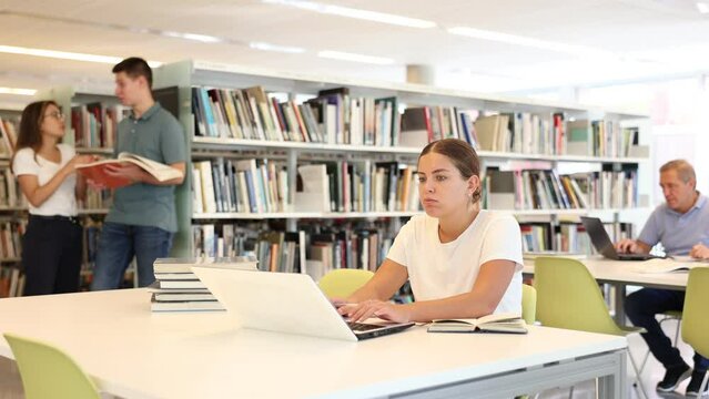 Portrait of positive woman with laptop and book in public library
