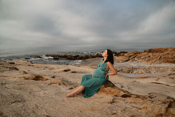 Pregnant woman posing in the long dress at Andalusian coast next to the sea