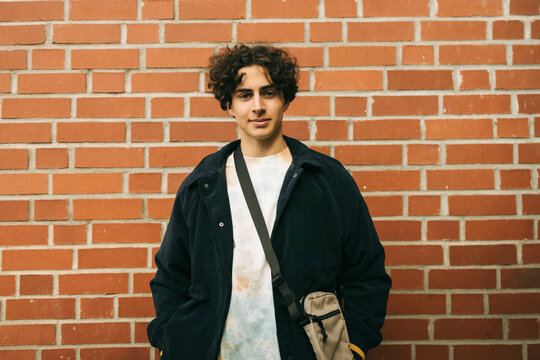 Portrait of teenage boy wearing jacket while standing against brick wall