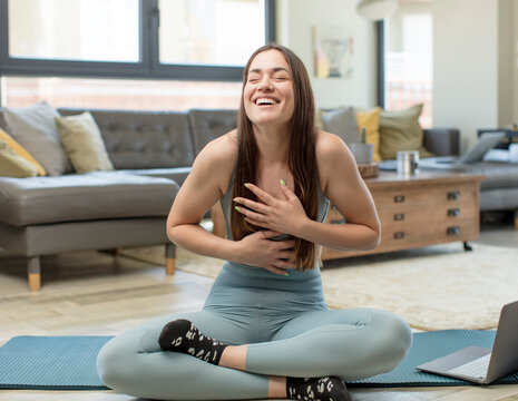 young adult woman practicing yoga laughing out loud at some hilarious joke, feeling happy and cheerful, having fun