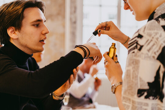 Non-binary person testing essential oil sample on male colleague's hand during event at convention center