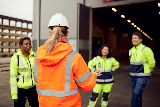 Rear view of female engineer in protective workwear discussing with workers at factory