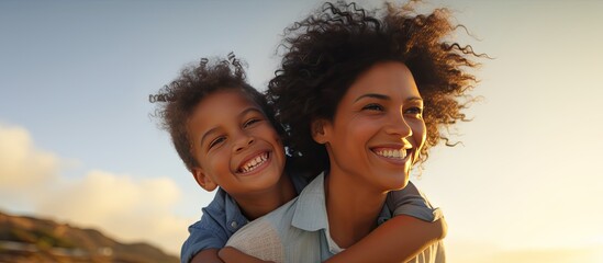 Happy African American mother carrying her son on her back at the beach under a blue sky during sunset