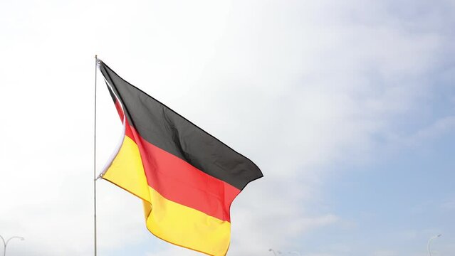 Black, red, and gold tricolor Bundesflagge, national symbol of idea of strong and united democratic Germany, culture and rich history waving on flagpole against backdrop of cloudy sky. High quality 4k