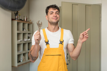 young handsome man smiling cheerfully, feeling happy and pointing to the side. handyman concept