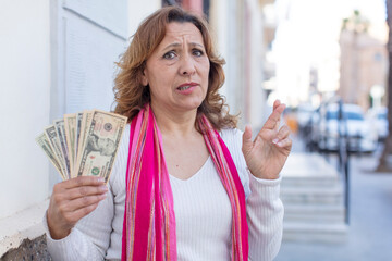 middle age pretty woman crossing fingers and hoping for good luck. dollar banknotes concept