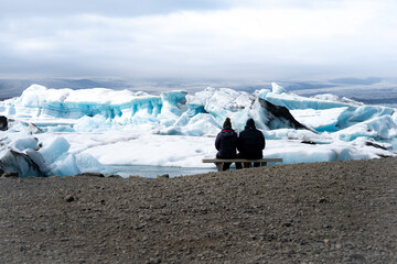 Two people sitting and watching Large ice cubes that breaks out of Garcia on a mountain in Iceland
