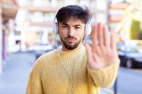 young handsome man looking serious showing open palm making stop gesture. listening music with headphones