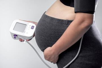 Close-up of pregnant woman checking her measures blood pressure with an electronic tonometer at home, Hypertension, severe pregnancy, headache, migraine concept.