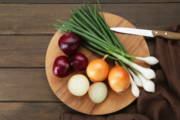 Board with different kinds of onions on wooden table, top view