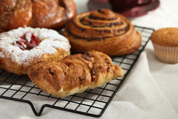 Different tasty freshly baked pastries on cooling rack, closeup