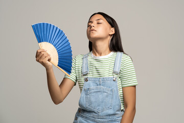 Overheated teenage girl holding bright fan in her hand. Tired teenager girl languishing from heat...