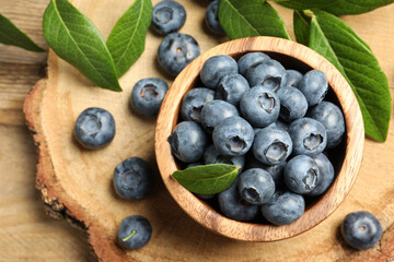 Bowl of tasty fresh blueberries with leaves on wooden table, flat lay. Space for text