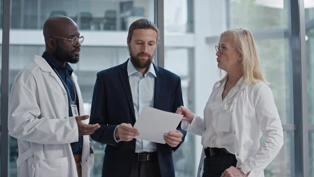 Medium shot of young entrepreneur discussing strategy of clinic growth and showing something in document to doctors