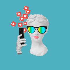 Antique statue's head in sunglasses holding mobile phone with like symbols from social media on...