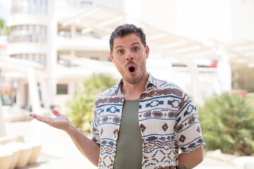 handsome man looking surprised and shocked, with jaw dropped holding an object with an open hand on the side