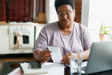 Portrait of puzzled upset serious overweight african american grandma in glasses reading paycheck...