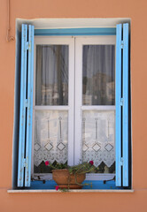 Greek Home with Blue Window Shutters ad Flower Pot in Symi, Greece