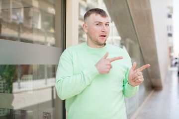 handsome man feeling shocked and surprised, pointing to copy space on the side with amazed, open-mouthed look