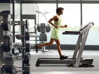 Obraz na płótnie Canvas Full length profile shot of an african american guy running on a treadmill at a gym