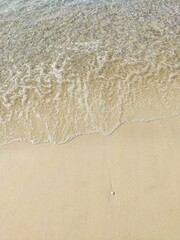 Transparent water on a smooth sandy beach with a lone pebble, top view