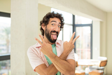 young crazy bearded man smiling and looking happy, friendly and satisfied, gesturing victory or peace with both hands