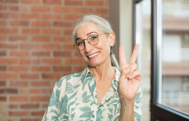 senior pretty woman smiling and looking happy, carefree and positive, gesturing victory or peace with one hand