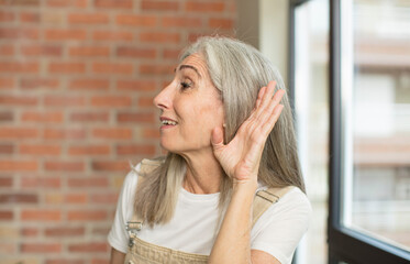 senior pretty woman looking happy, listening, trying to hear a secret conversation or gossip,...