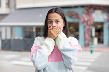 pretty hispanic woman covering mouth with hands with a shocked, surprised expression, keeping a secret or saying oops