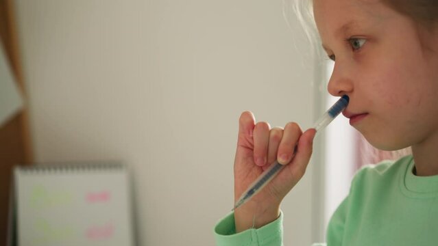 Pensive schoolchild presses pen tip to nose and purses lips considering task. Diligent little girl do homework. Educational process in primary school closeup