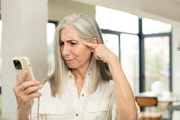 pretty senior woman looking surprised, realizing a new thought, idea or concept. smartphone concept