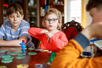 Family playing board game at home. Kids play strategic game. Little sister girl and two school brothers boys. Fun indoor activity. Siblings bond. Educational toys.