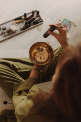 Woman playing on Tibetan singing bowl while sitting on yoga mat. Vintage tonned. Soft focus blurred...
