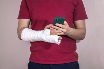 A man in a red T-shirt with a broken arm in a cast holds and uses a phone Close-up