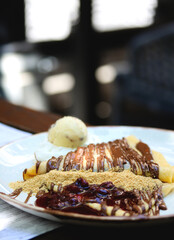 Thin pancake with chocolate cream. Pancakes with chocolate paste, hazelnuts, cherry sauce and a scoop of ice cream on a white plate on a restaurant table. Crepes with chocolate cream