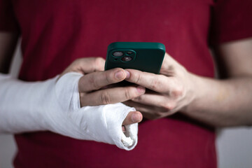 A man in a red T-shirt with a broken arm in a cast holds and uses a phone Close-up