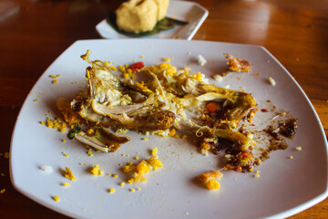 Kitchen waste on white plate, food scraps, left over, discarded food and piles of chicken bones.