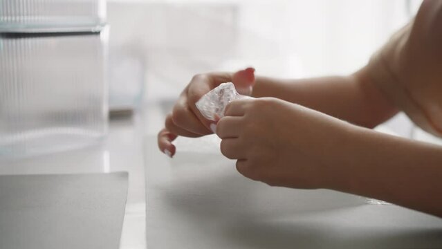 Female hands with white fingernails press on protective film popping bubbles. Young woman spends free time sitting at kitchen table with food containers closeup