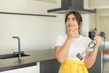 young woman smiling with a happy, confident expression with hand on chin. chef with hand blender
