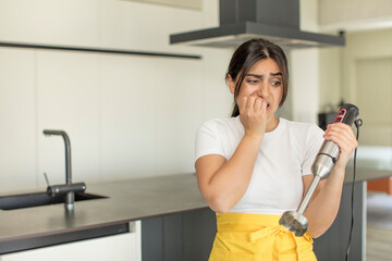 young woman feeling scared, worried or angry and looking to the side. chef with hand blender