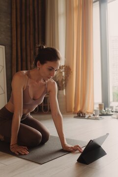 Young woman in sportswear exercises doing work out and using tablet to watch yoga video tutorial. Distant training with personal trainer, social distance, online concept. Soft focus and noise effect
